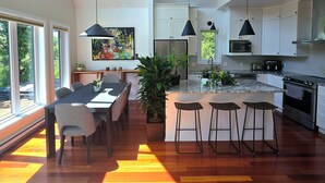 A modern kitchen with a central island, pendant lighting, and a dining area with a view of the outdoors.