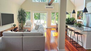 A spacious living room with a large sofa, a TV, and a dining area with bar stools.