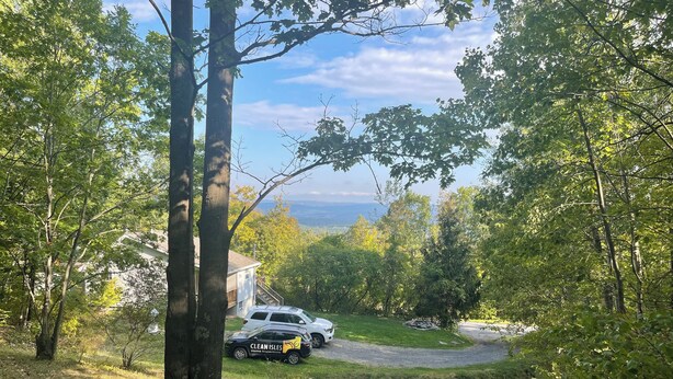 A residential area with a driveway, a white house, and a black vehicle parked in front. - Cozy 2-bedroom cabin in lovely Acra with cool AC (Acra)