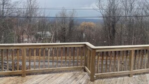 A wooden deck with a railing, overlooking a forested area with bare trees and a distant view of a mountain range. - Cozy 2-bedroom cabin in lovely Acra with cool AC (Acra)