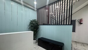 A reception area with a marble floor, a reception desk, a potted plant, and a staircase with a black railing. - Urban Hive By T And M Hotels (Haridwar)