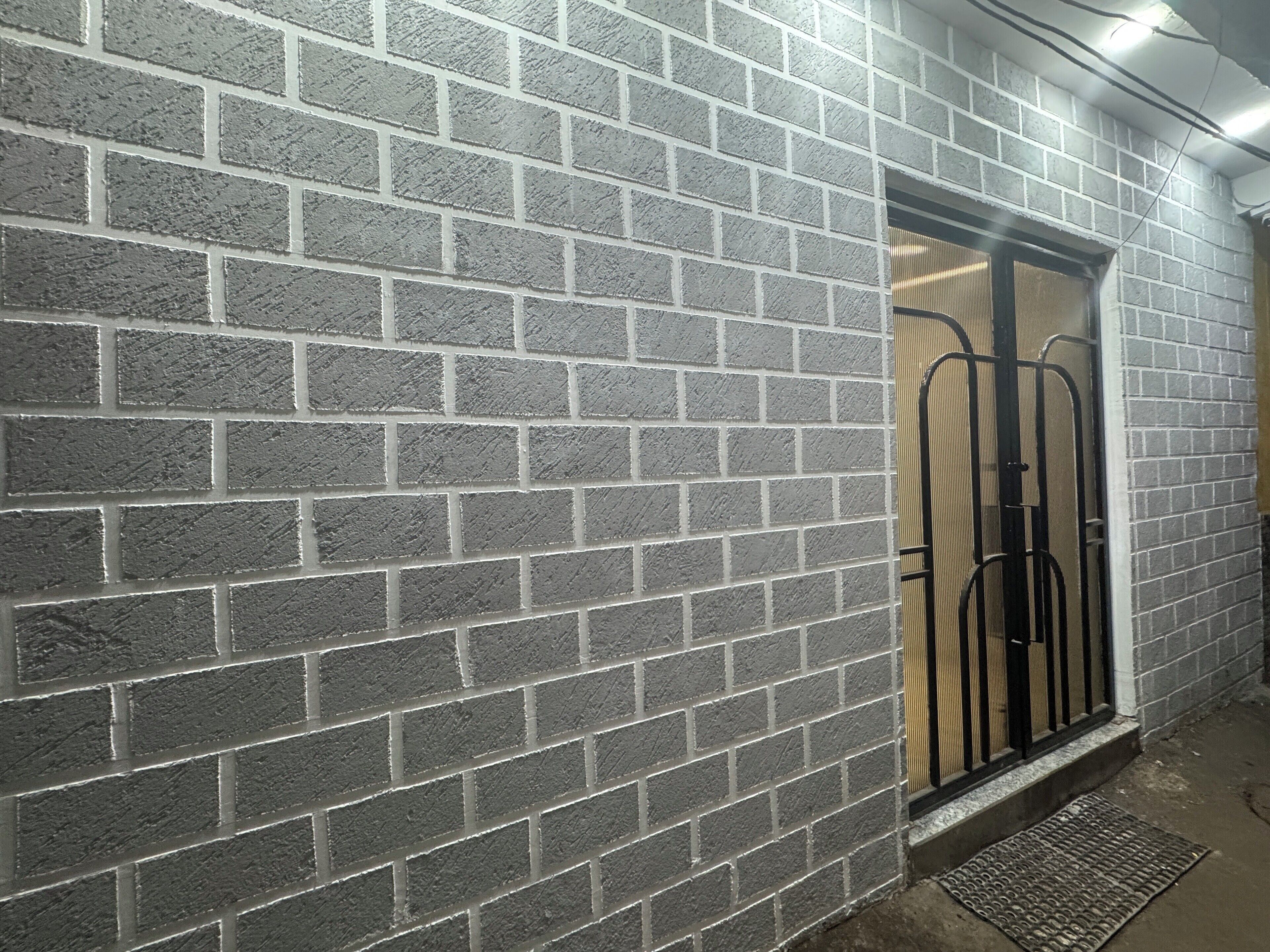 Un muro de ladrillo con una reja metálica y un escalón que lleva a una puerta.