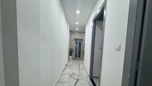 A hallway with white walls and a marble floor leading to a door. - Urban Hive By T And M Hotels (Haridwar)
