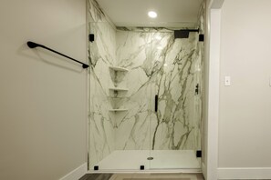 Une salle de bain moderne avec une douche à parois de verre, des murs en marbre et un porte-serviettes noir.