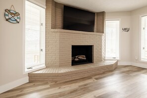 Une pièce avec une cheminée en briques, des murs blancs et un plancher en bois.