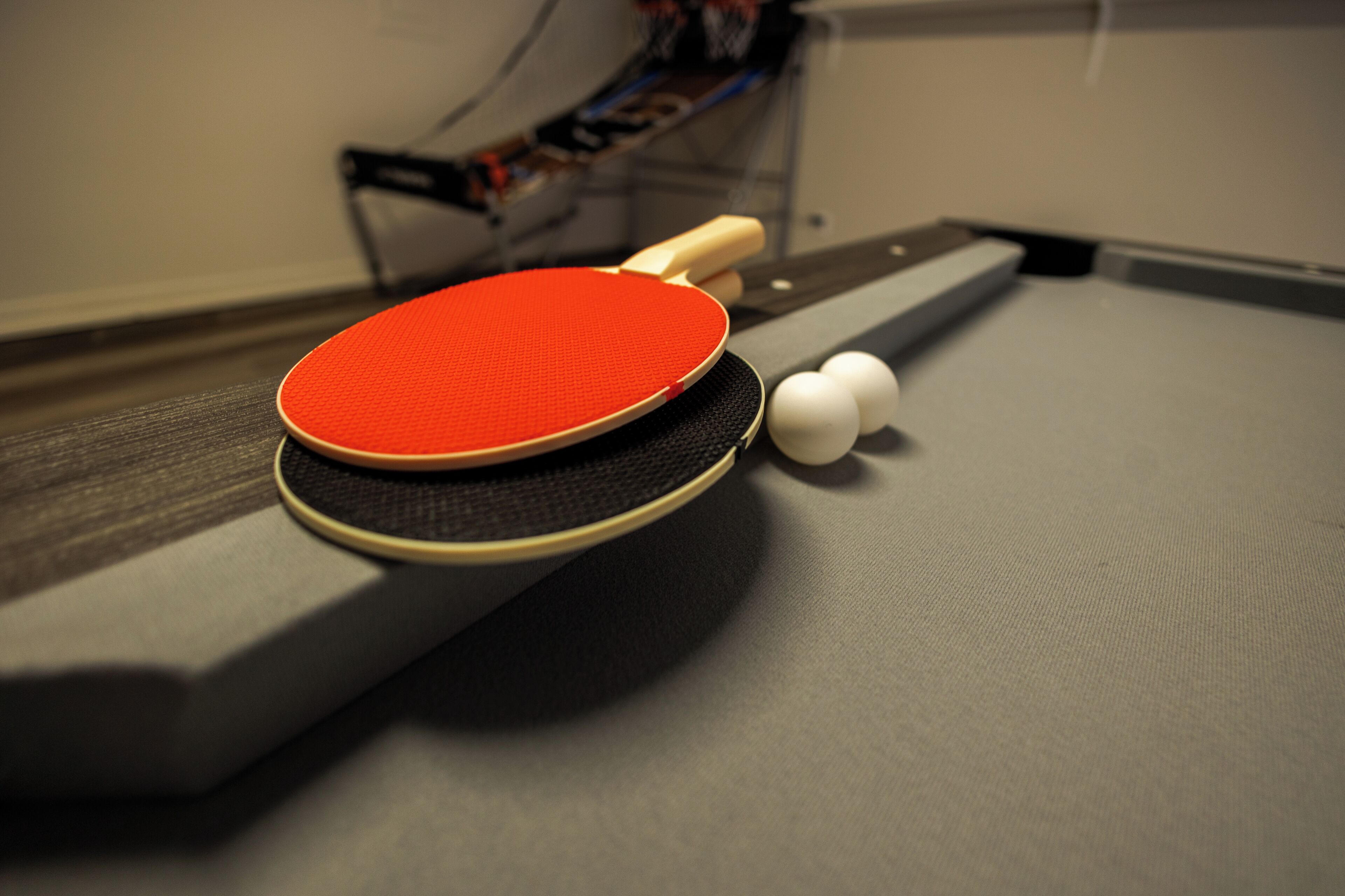 A table with a red table tennis paddle, a black table, and two white table tennis balls.