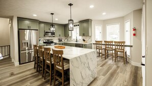 A modern kitchen with a marble island, wooden chairs, and stainless steel appliances. - Remodeled Lakefront Retreat with Hot Tub (Lyon County)