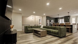 A modern living room with a sectional sofa, a coffee table, and a TV on a black stand. - Remodeled Lakefront Retreat with Hot Tub (Lyon County)