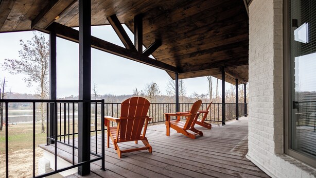 A covered deck with wooden chairs and a view of a lake. - Remodeled Lakefront Retreat with Hot Tub (Lyon County)
