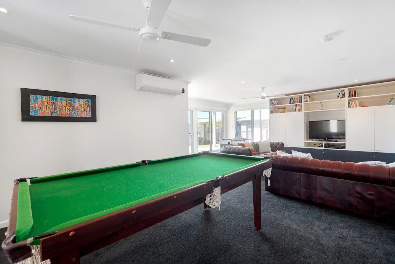 Ein Billardtisch in einem Wohnzimmer mit Sofa und Fernseher.
