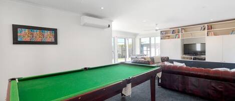 Ein Billardtisch in einem Wohnzimmer mit Sofa und Fernseher.