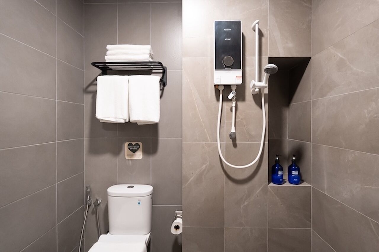 A modern bathroom with a toilet, a towel rack, a shower unit, and two bottles of shampoo.
