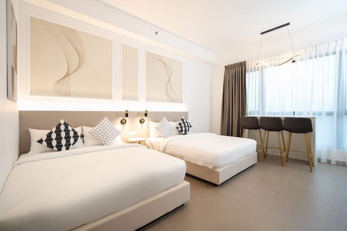 A modern hotel room with two beds, a desk with chairs, and abstract wall art.