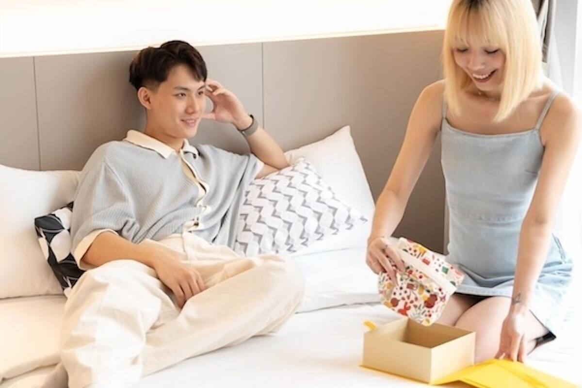 A man and a woman sitting on a bed in a hotel room.