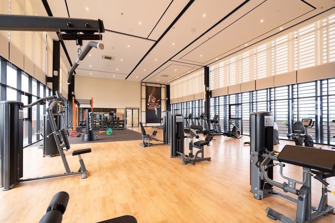 A spacious gym with various exercise machines, large windows, and a wooden floor.