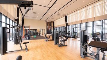 A spacious gym with various exercise machines, large windows, and a wooden floor.