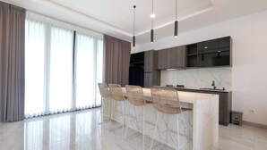 A modern kitchen with a marble countertop, four bar stools, and pendant lighting. - Bellevue Villa Canggu (Canggu)