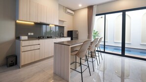 A modern kitchen with a central island, bar stools, and a view of a swimming pool through large windows. - Bellevue Villa Canggu (Canggu)
