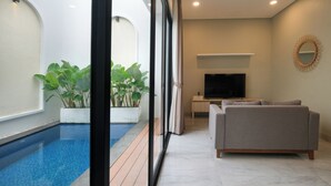 A modern living room with a pool, a grey sofa, and a flat-screen TV. - Bellevue Villa Canggu (Canggu)