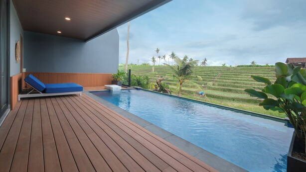 A modern pool area with a wooden deck, a blue lounge chair, and a view of terraced fields. - Bellevue Villa Canggu (Canggu)