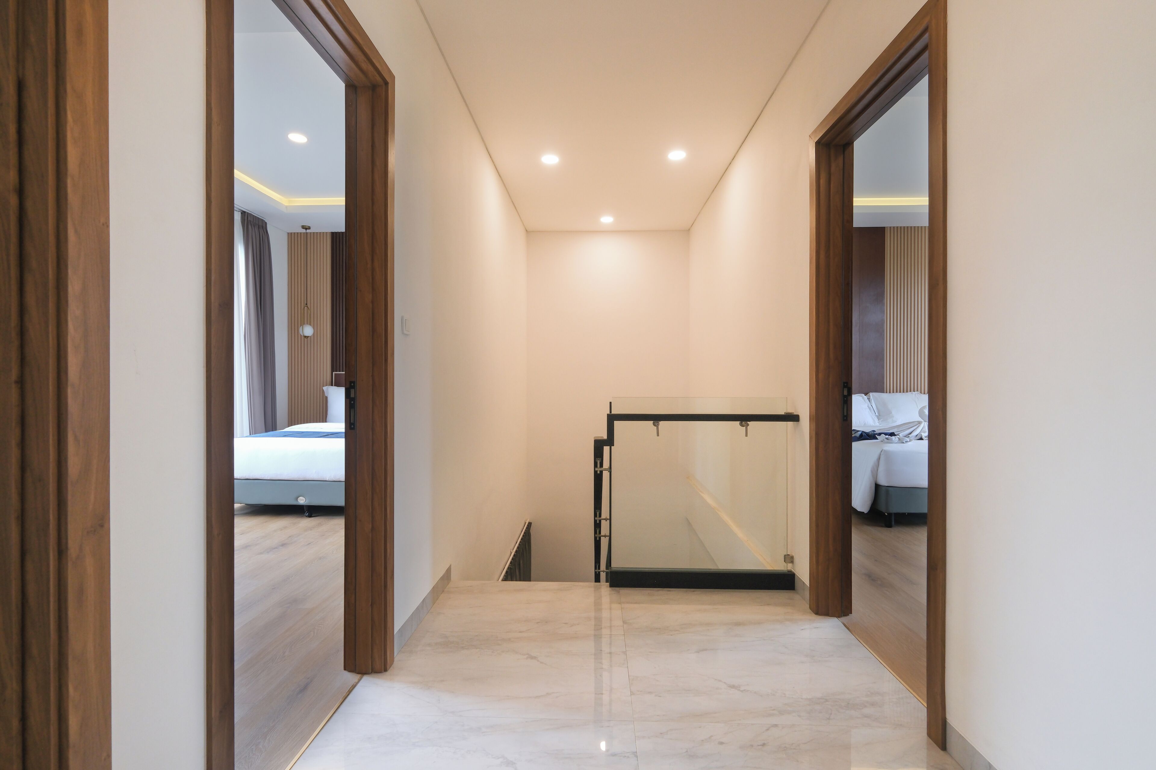 A modern hotel hallway with a glass partition, wooden flooring, and a ceiling with recessed lighting.