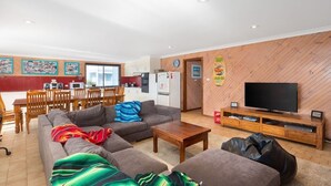 En moderne stue med sofa, sofabord og tv-møbel. Der er et spiseområde med bord og stole.