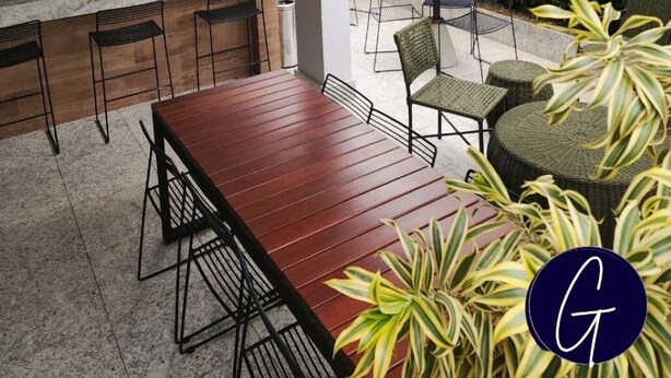 A modern outdoor kitchen area with a wooden table and chairs, a round dining table, and a black grill. - Beautiful studio apartment 400m from Allianz Parque. (São Paulo)