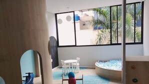 A play area with a wooden structure, a white table with chairs, and a view of palm trees through large windows. - Beautiful studio apartment 400m from Allianz Parque. (São Paulo)