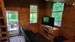 A cabin with a wooden interior, a television on a wooden stand, a bench, and a ladder. - Cute 1-bedroom off grid cabin in Winfield for a cozy getaway (Winfield)