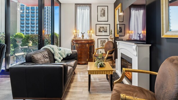 Ein modernes Wohnzimmer mit einer Couch, einem Sessel, einem Kamin und Blick auf eine Stadtlandschaft durch große Fenster.