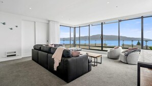 Una sala moderna con un sofá negro, sillones orejeros grises y vistas al mar.