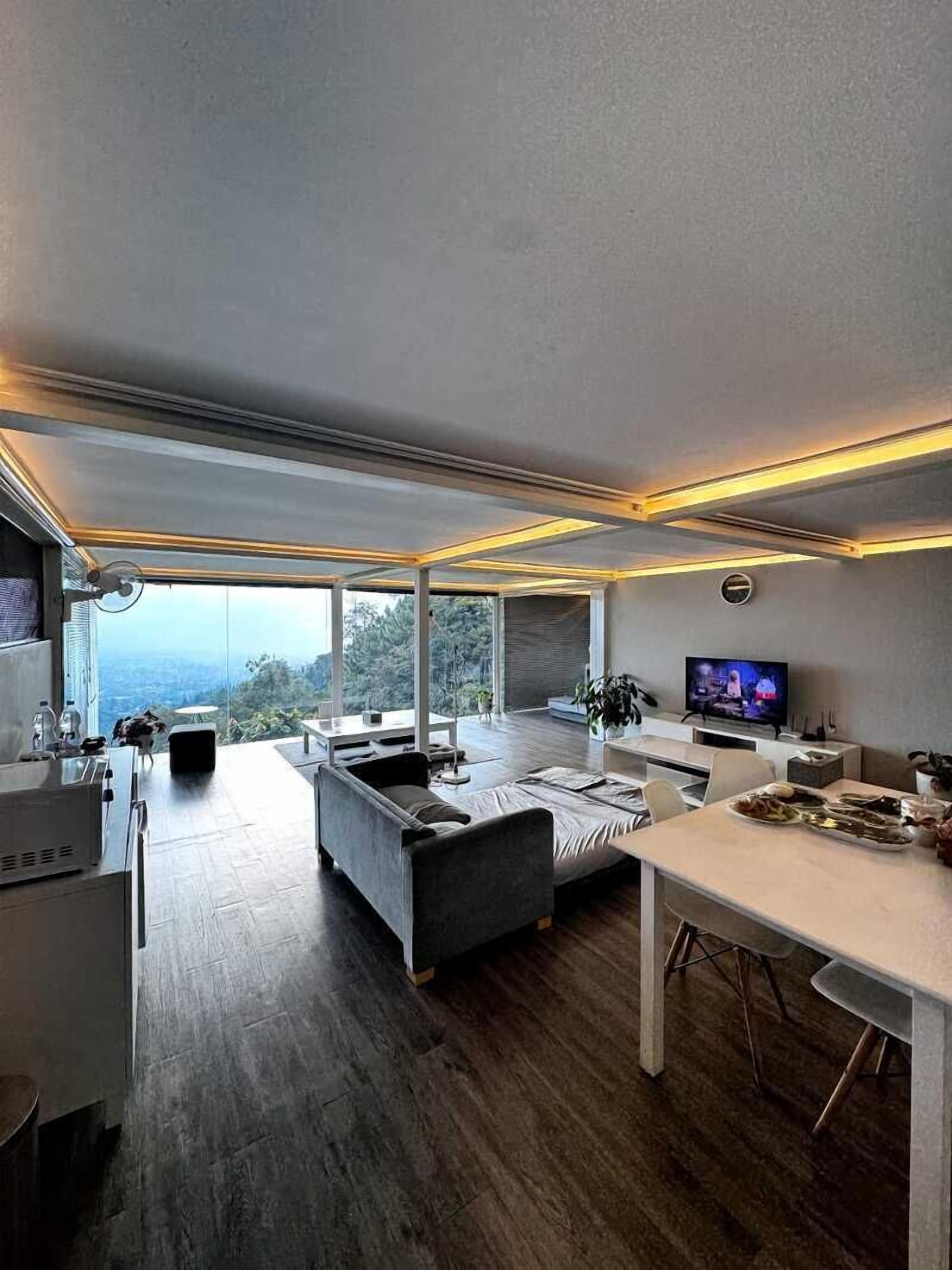 A modern kitchen with a dining area, large windows, and a flat-screen TV.