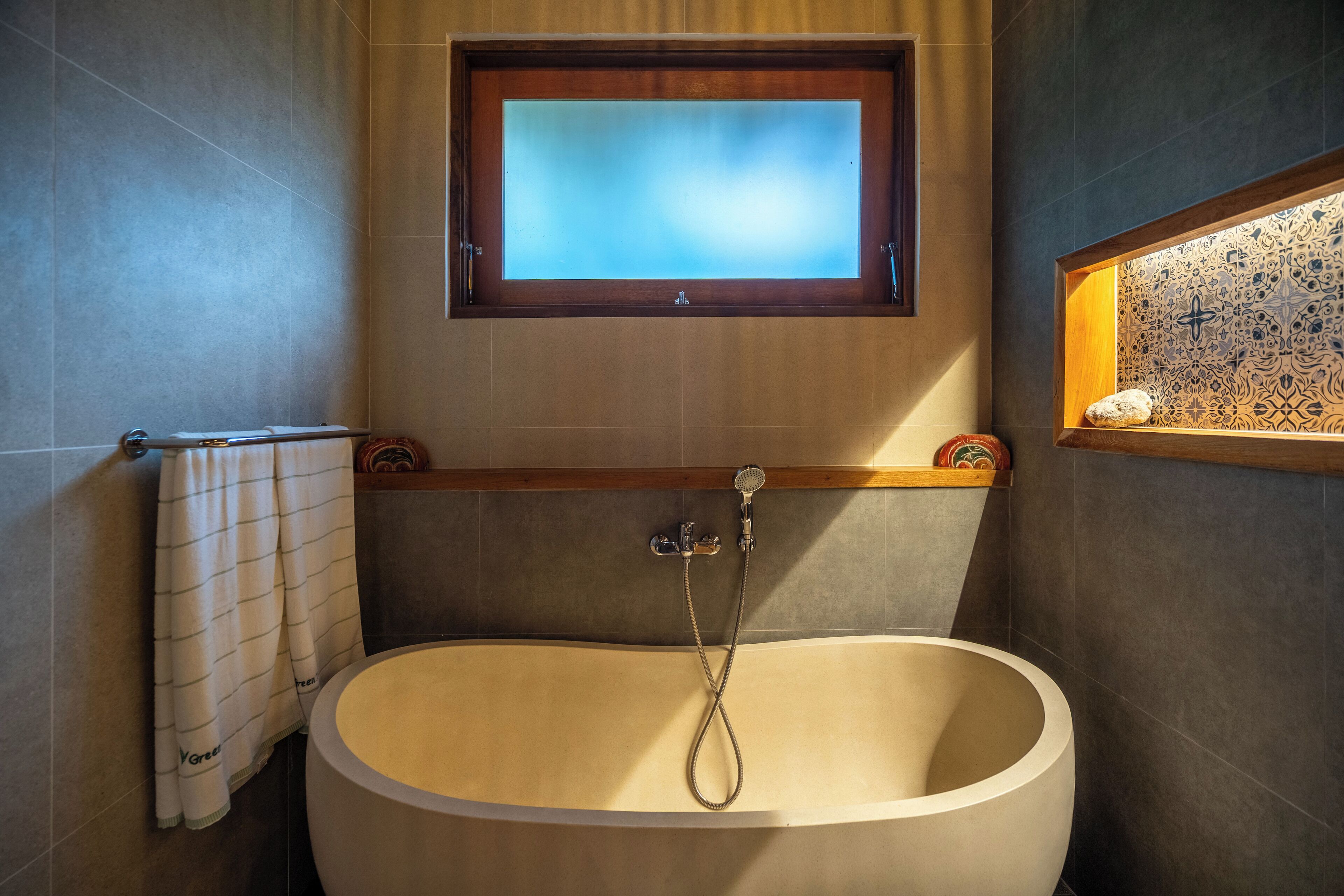 A modern bathroom with a freestanding bathtub, a window above the tub, and a decorative tile shelf.