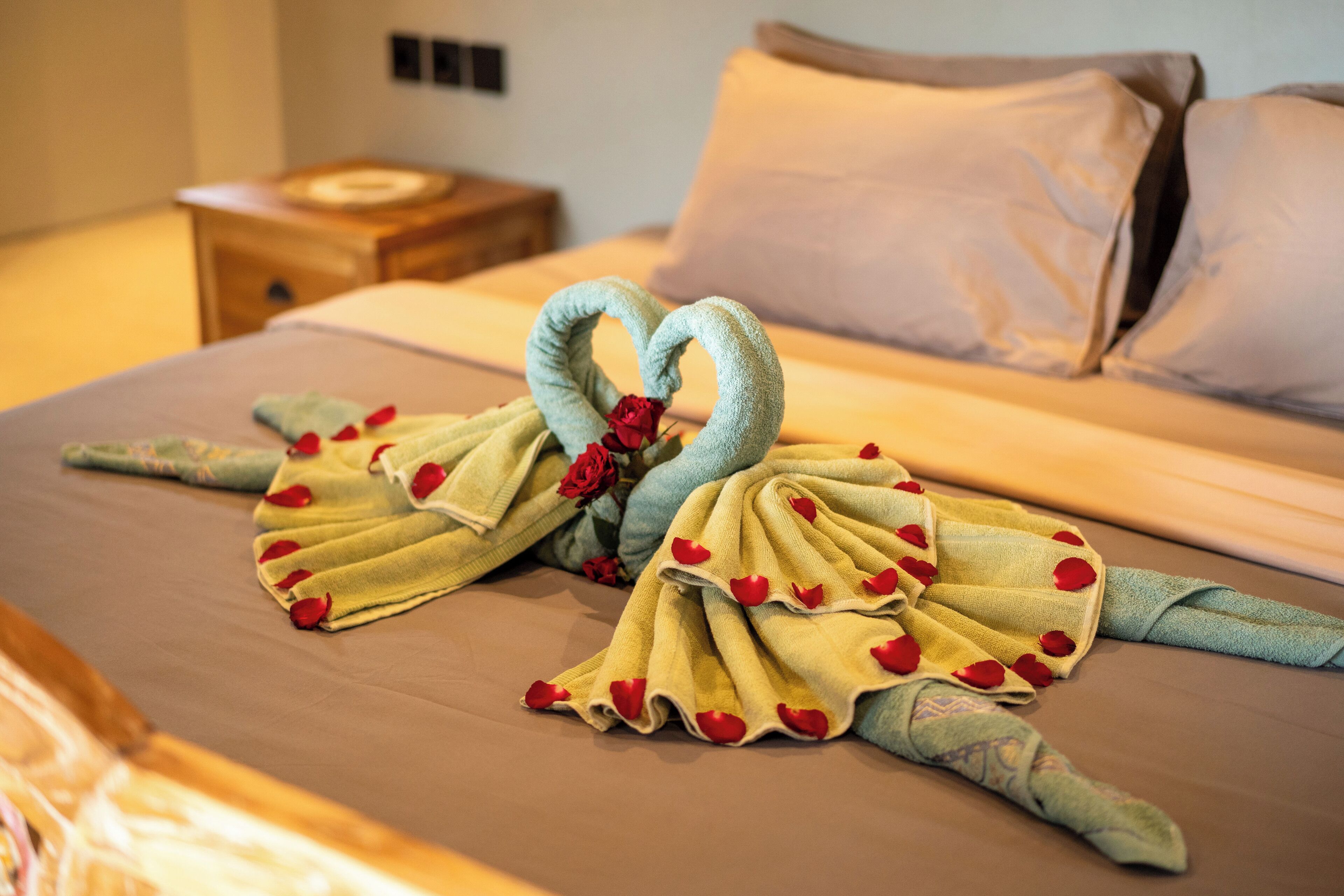 Una cama con una toalla dispuesta en forma de corazón y pétalos de rosa.