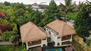 Un resort tropical con dos cabañas de techo de paja, una piscina y abundante vegetación.