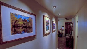 A hallway with framed landscape paintings on the wall, wooden flooring, and a door at the end.