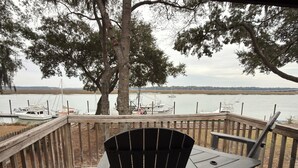 A wooden deck with a view of a lake, a boat docked, and a chair.