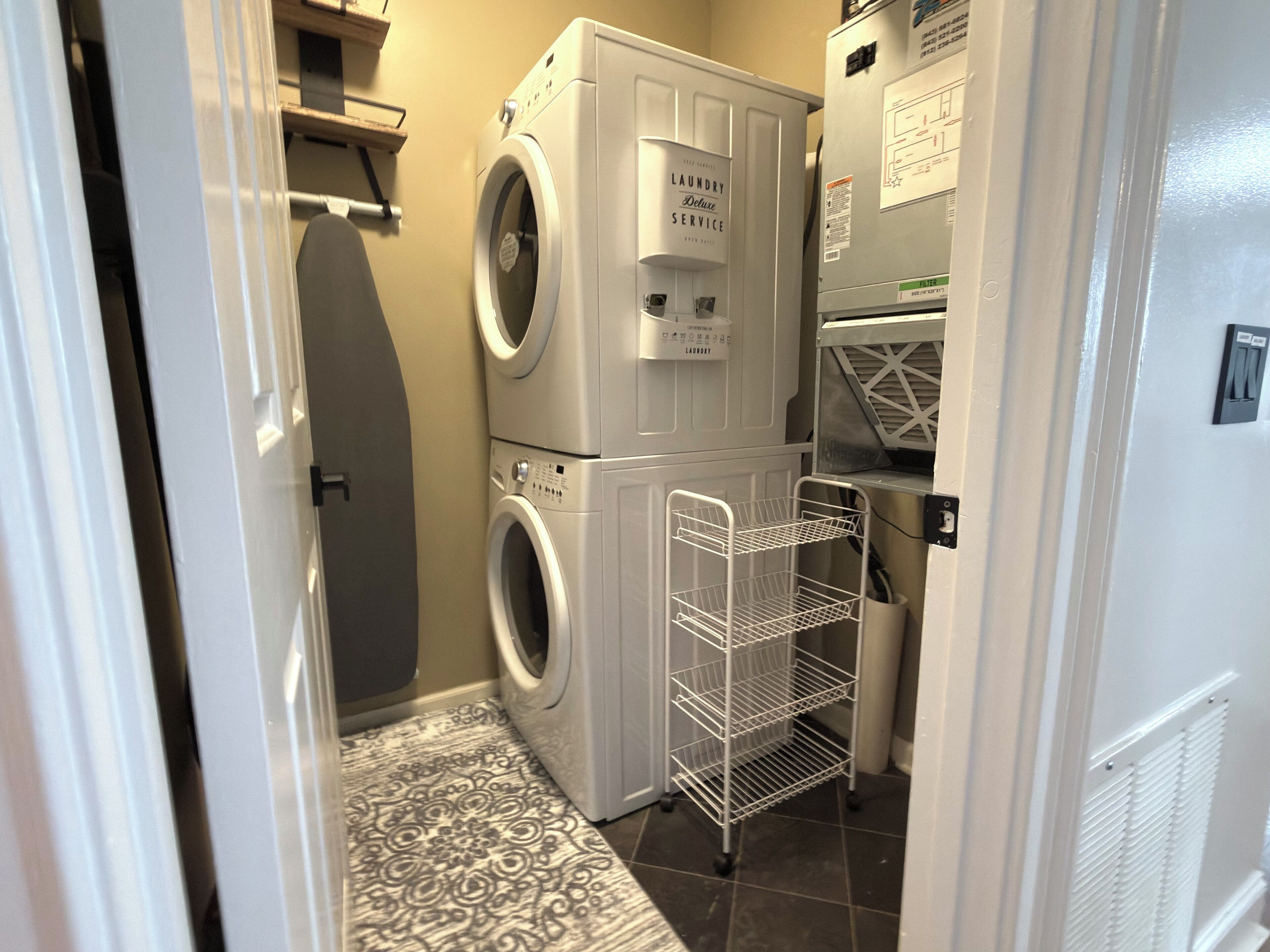 A laundry room with a front-loading washer and dryer, a metal shelf unit, and a tiled floor.