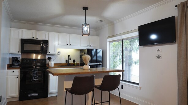 A modern kitchen with white cabinets, a black stove, and a bar area with two stools.