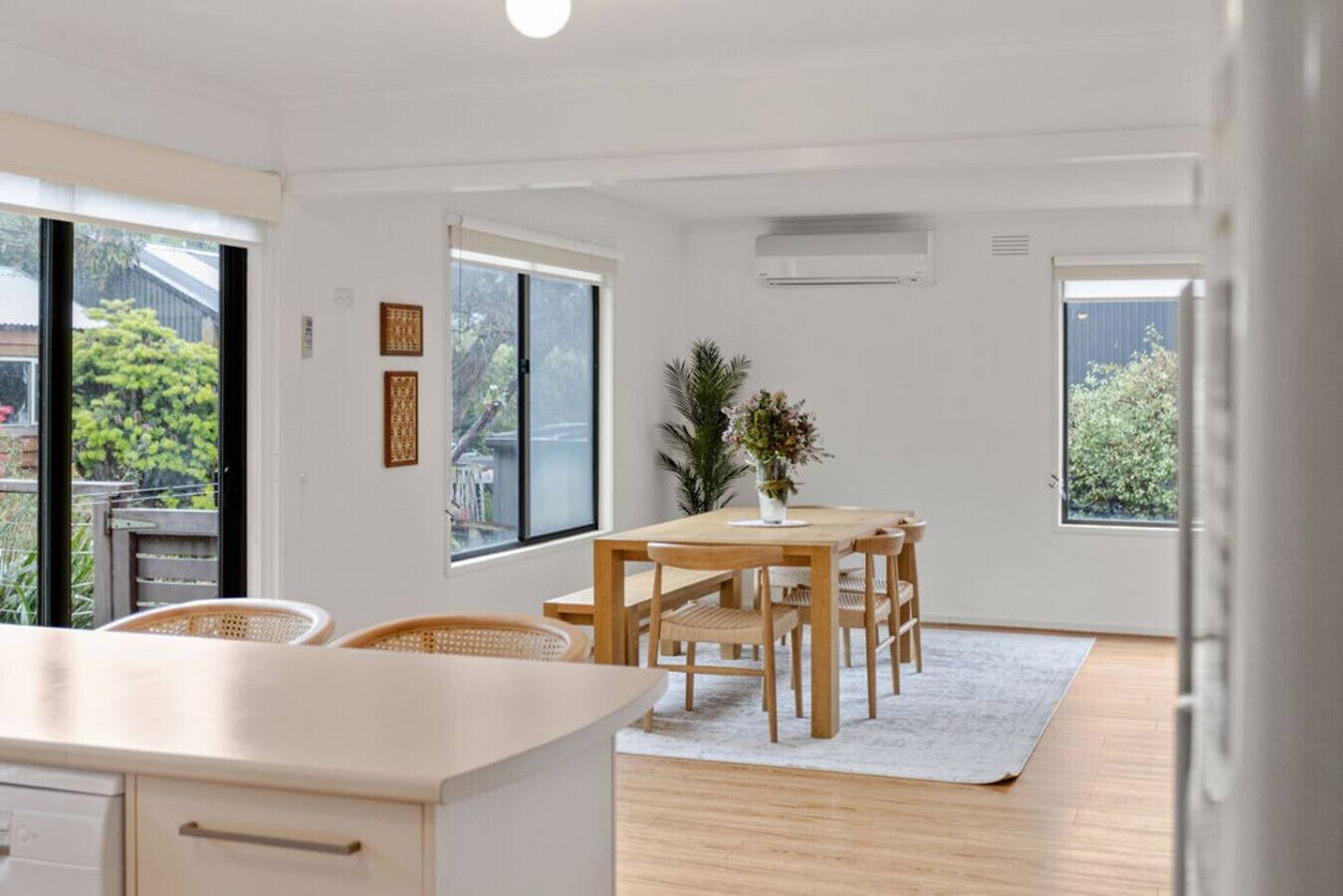 Eine moderne Küche mit Holzarbeitsplatte und Schränken, ein Essbereich mit Holztisch und Stühlen sowie große Fenster mit Blick auf Grünflächen.