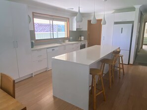 A modern kitchen with a large island, wooden stools, and white cabinetry. -  Coastal Palms  Relaxing pet friendly accommodation with pool (Yamba)