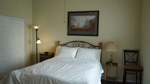 A neatly made bed in a room with a framed landscape painting above it, a bedside lamp, and a chair with a cushion. - 3-bedroom house in lovely Wildomar with cool AC (Wildomar)