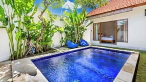 A swimming pool with a tiled deck, surrounded by lush greenery and a white building with a tiled roof. - The Wina Ambengan Canggu (Canggu)
