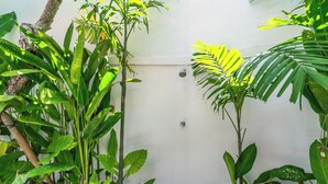 A corner of a room with a white wall, a shower, and various green plants. - The Wina Ambengan Canggu (Canggu)