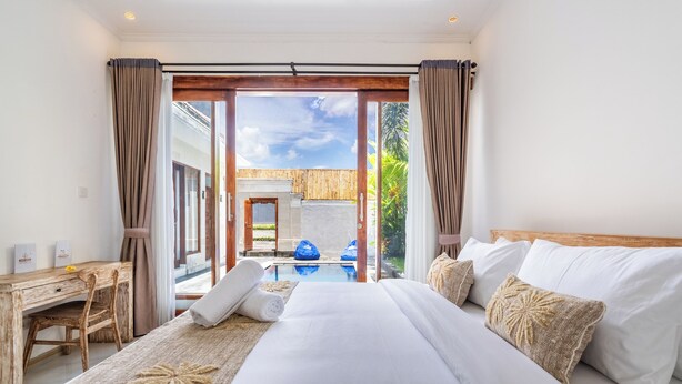 A spacious bedroom with a large bed, a wooden desk, and a view of a swimming pool and outdoor area. - The Wina Ambengan Canggu (Canggu)