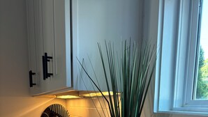 Una cucina con mobili bianchi, un piano di lavoro bianco, un piatto decorativo e un vaso con piante verdi.