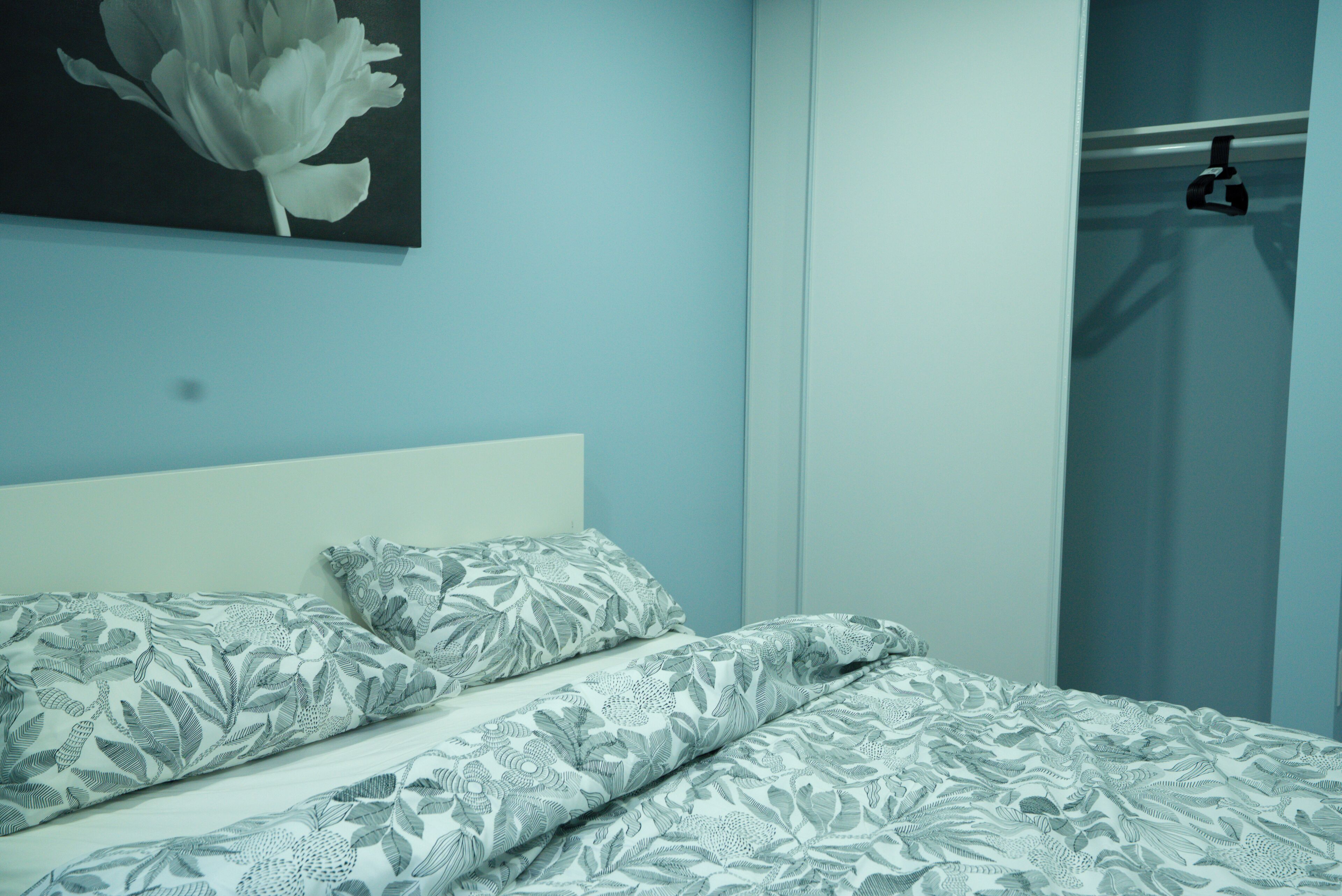 Un dormitorio con una cama, un almohadón, una obra de arte en la pared y un armario con puerta.