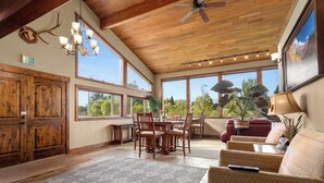 A spacious room with a wooden ceiling, large windows, a dining area, and a seating area with a sofa and a table. - Duck Inn Lodge (Whitefish)