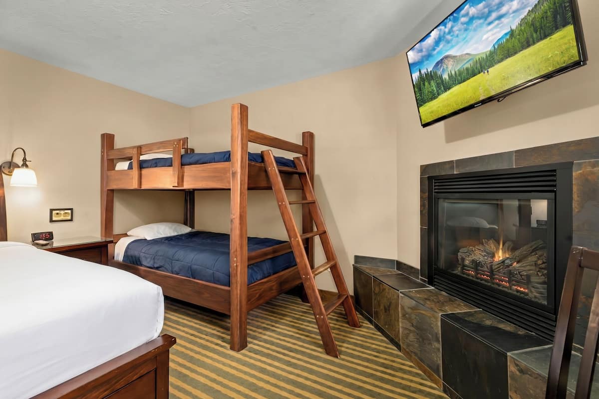 A bunk bed with a ladder, a flat bed, a fireplace, and a television on the wall.