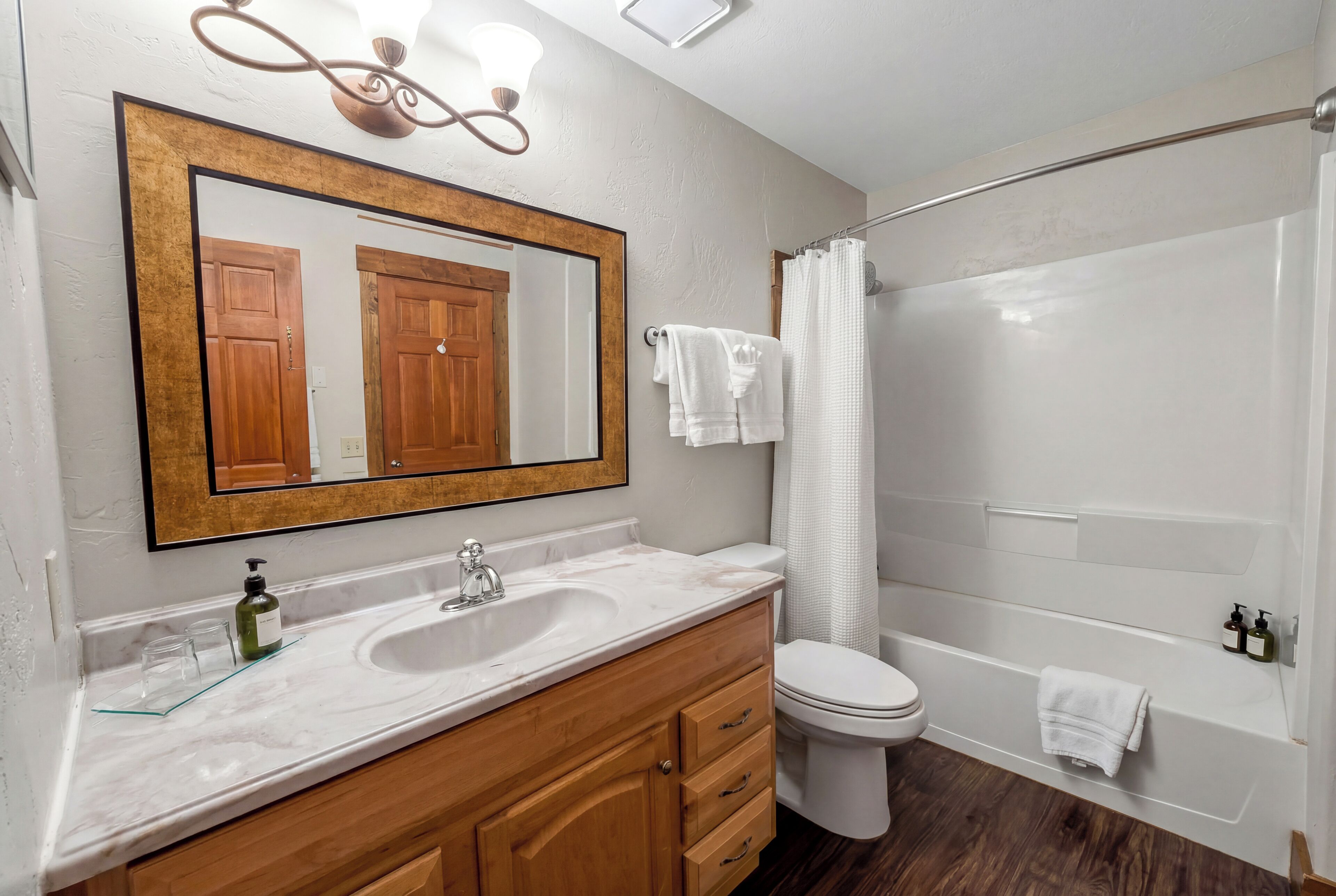 A bathroom with a large mirror, wooden vanity, white sink, toilet, and bathtub.
